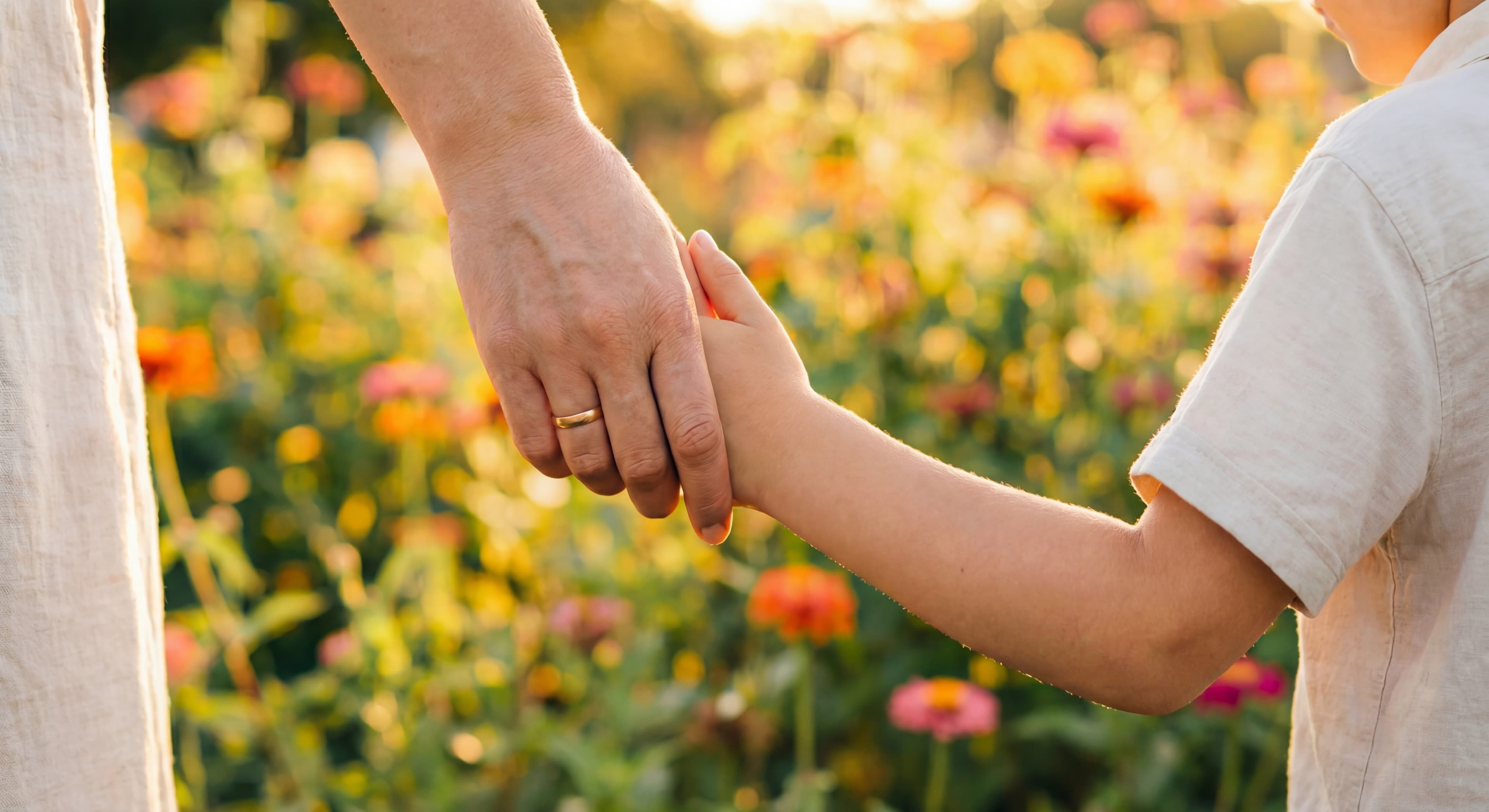 Elternteil hält Hand eines Kindes in einem Blumengarten